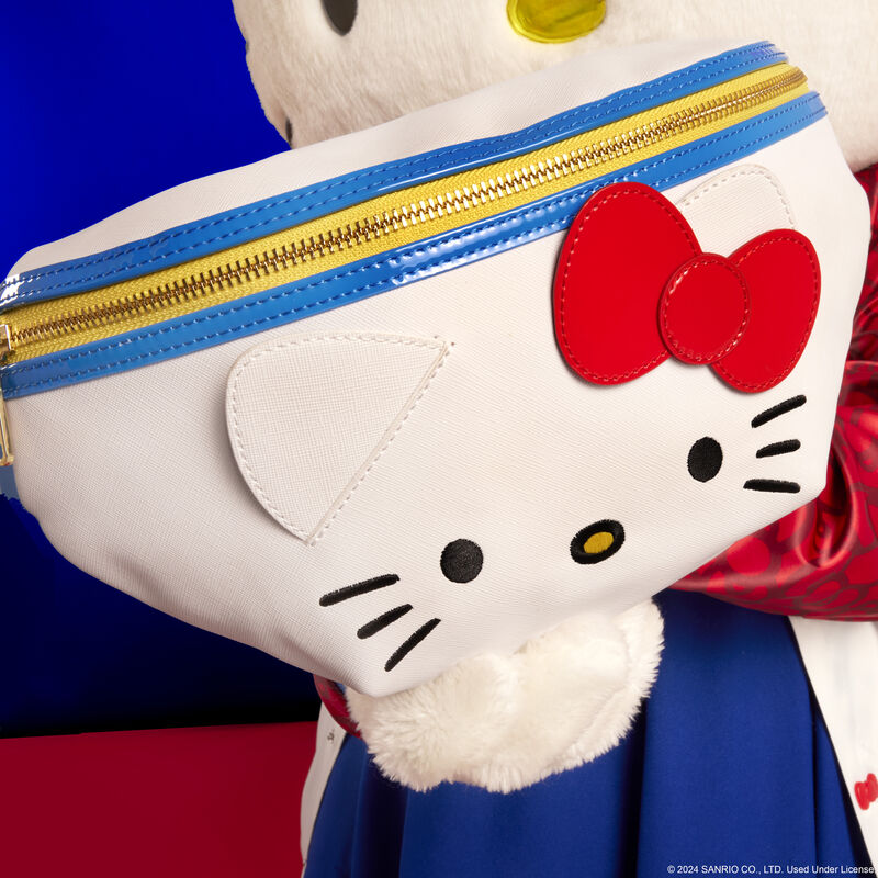 Hello Kitty holding the Loungefly Hello Kitty 50th anniversary cosplay convertible belt bag out to camera, showing off her embroidered facial details and 3D ears and bow on the bag
